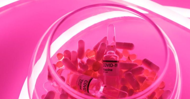 COVID Recovery - From above of glass bowl filled with pills and ampoules with vaccine for COVID 19 in pink bright neon light